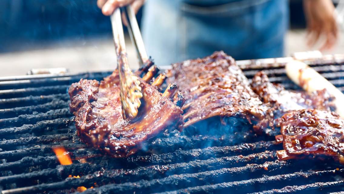 A close-up of someone cooking ribs on the grill.