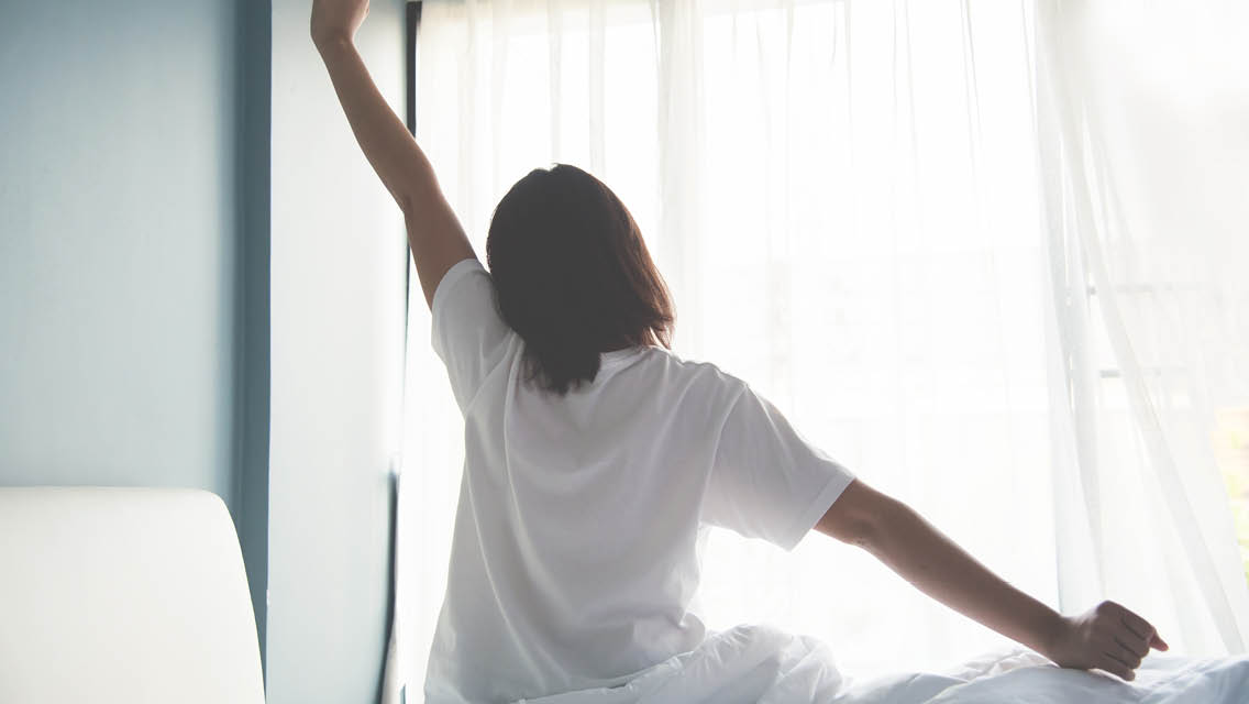 a woman stretches as she gets out of bed