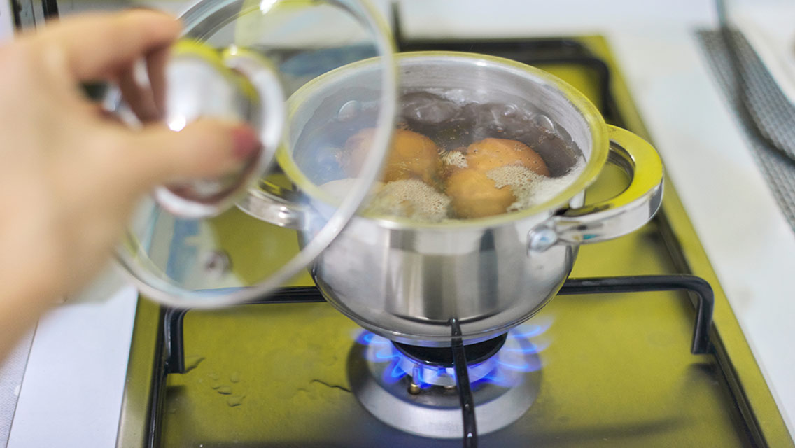 A person holds a lid above a pot of boiling eggs.