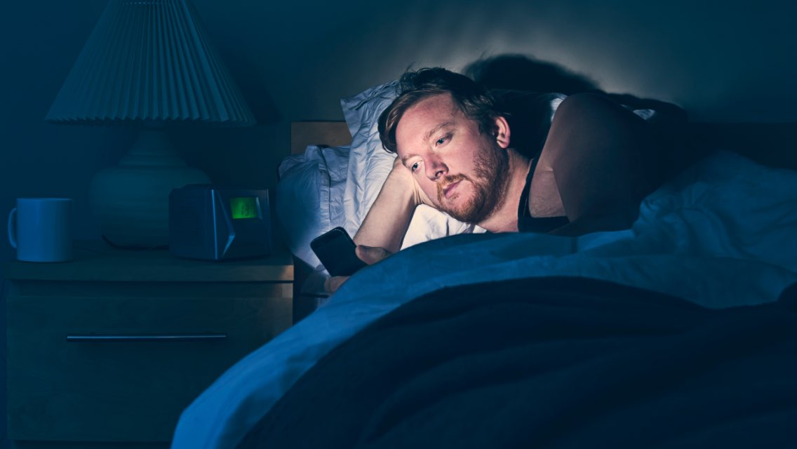 A man laying in bed awake at night staring at his phone.