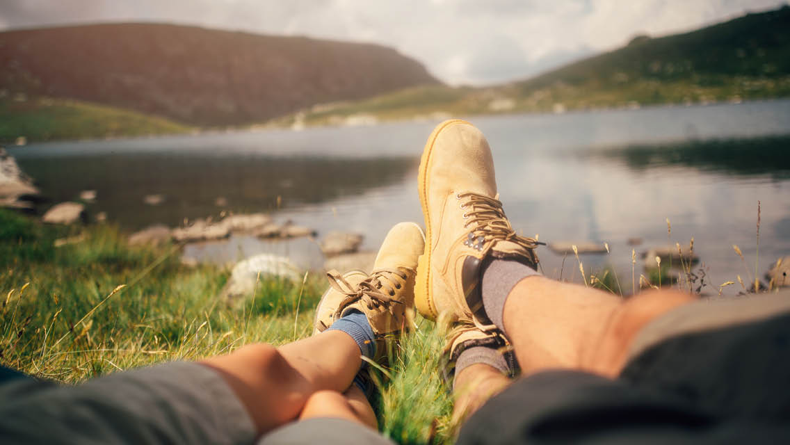 two sets of feet with hiking boots overlooking a mountain lake