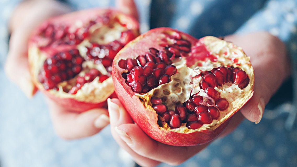 a person holds a pomegranate cut in half