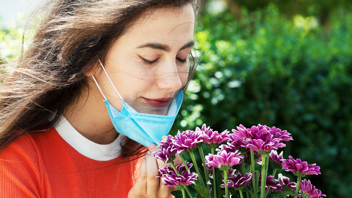a woman pulls a face mask away and smells flowers