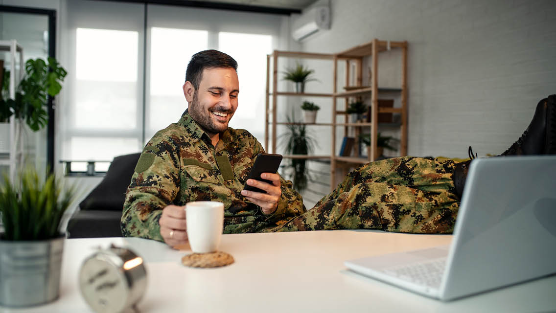 a man wearing military fatigues talks and laughs on his phone