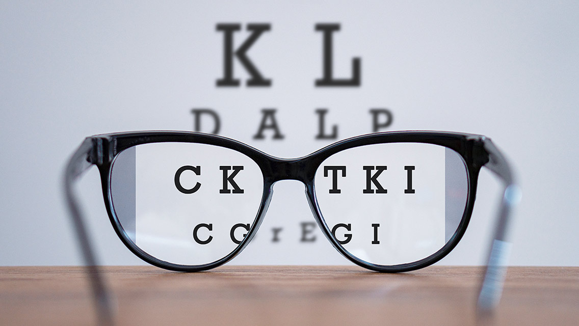 A pair of black glasses with a vision chart in the background