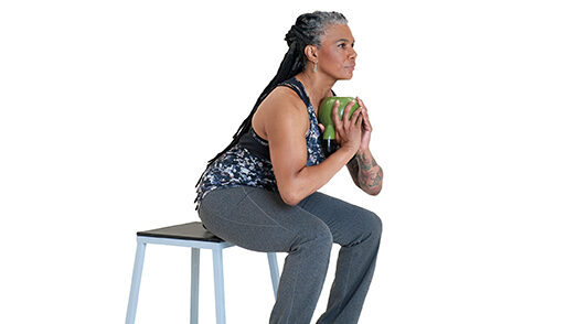 A woman sitting on a bench holding a weight with both hands.