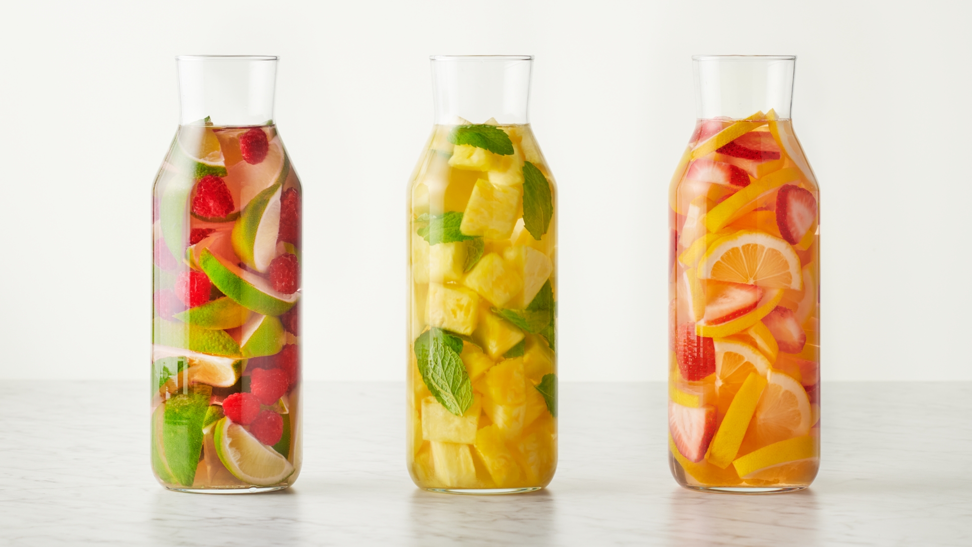 Three glass bottles of water infused with fruit and herbs.