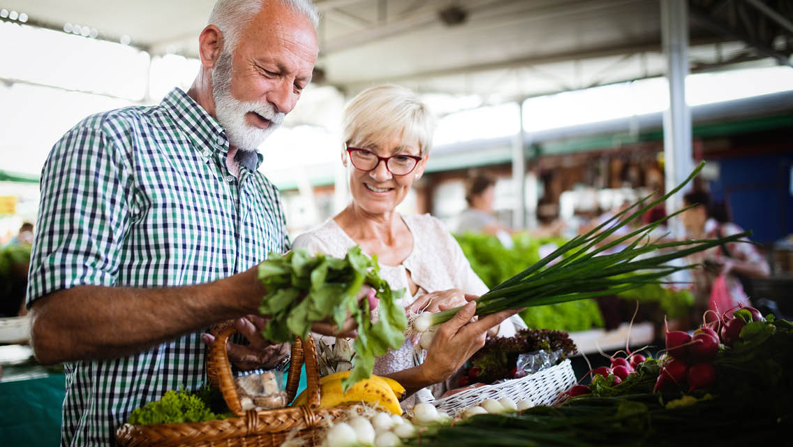 a senior aged couple shops for produce at a farmers market