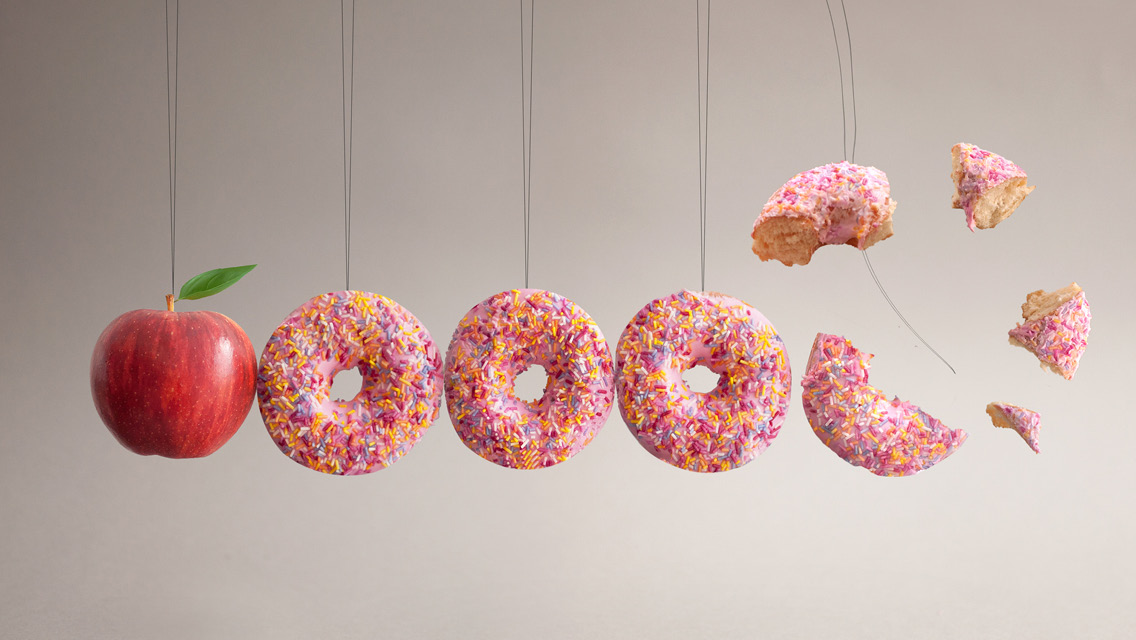 an apple and donuts hanging on strings like a pendulum