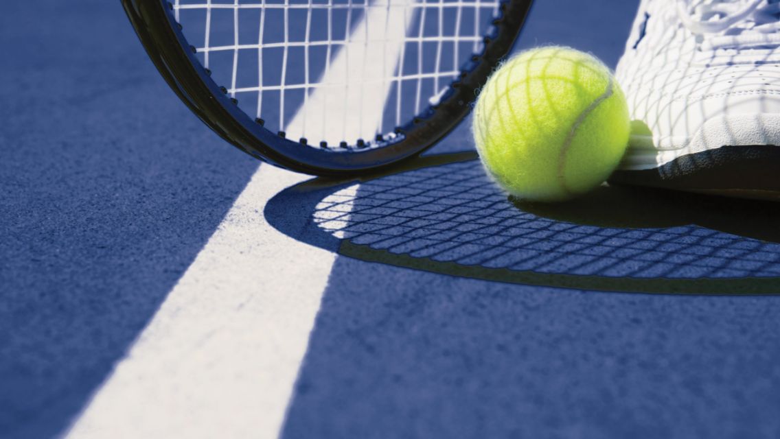 A close up shot of a tennis shoe, tennis ball, and tennis racquet on a tennis court.