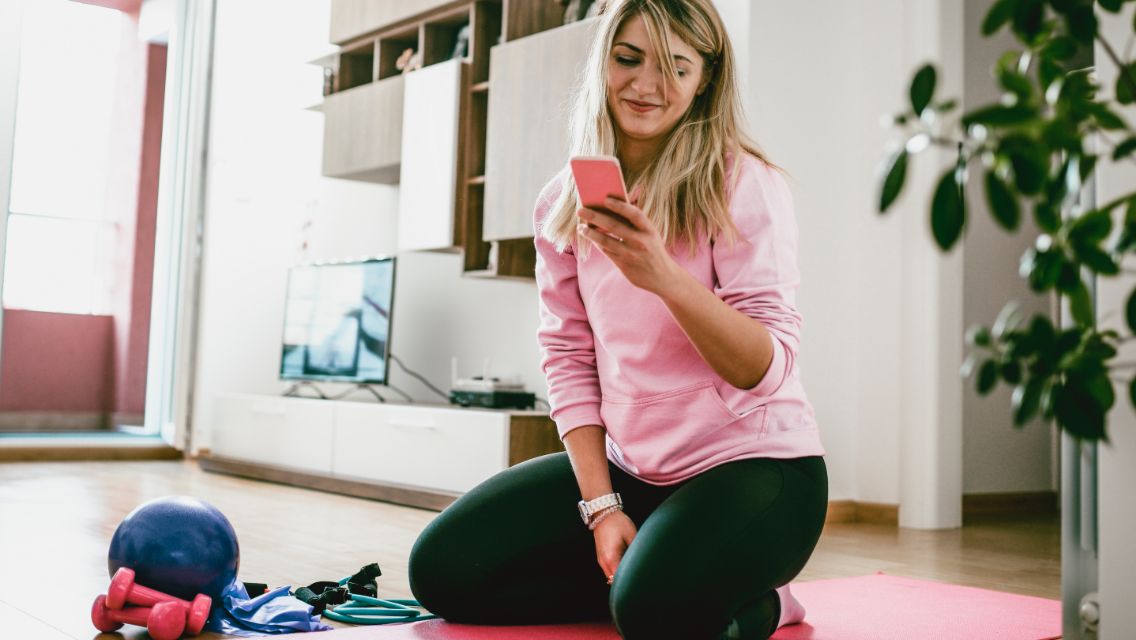A woman distracted on her phone during an attempt to work out at home.