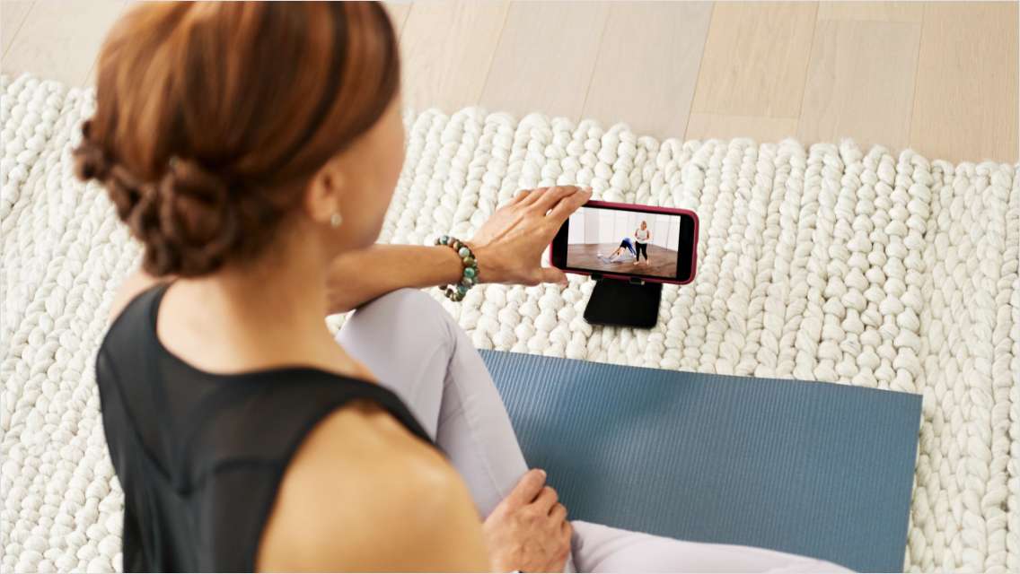 A woman looking at a workout video on a phone screen while at home.