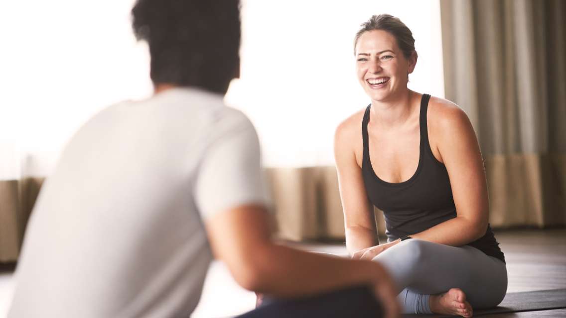 Two individuals talking and smiling in a yoga class.