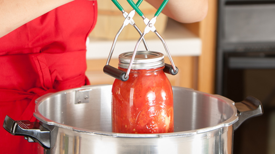 a person sets a jar of canned tomato sauce in a pot of boiling water