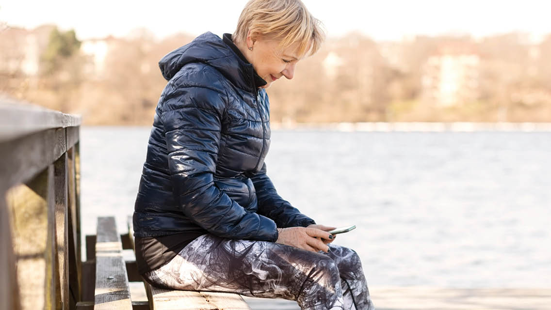 a woman sits on a dock looking at her phone in her lap