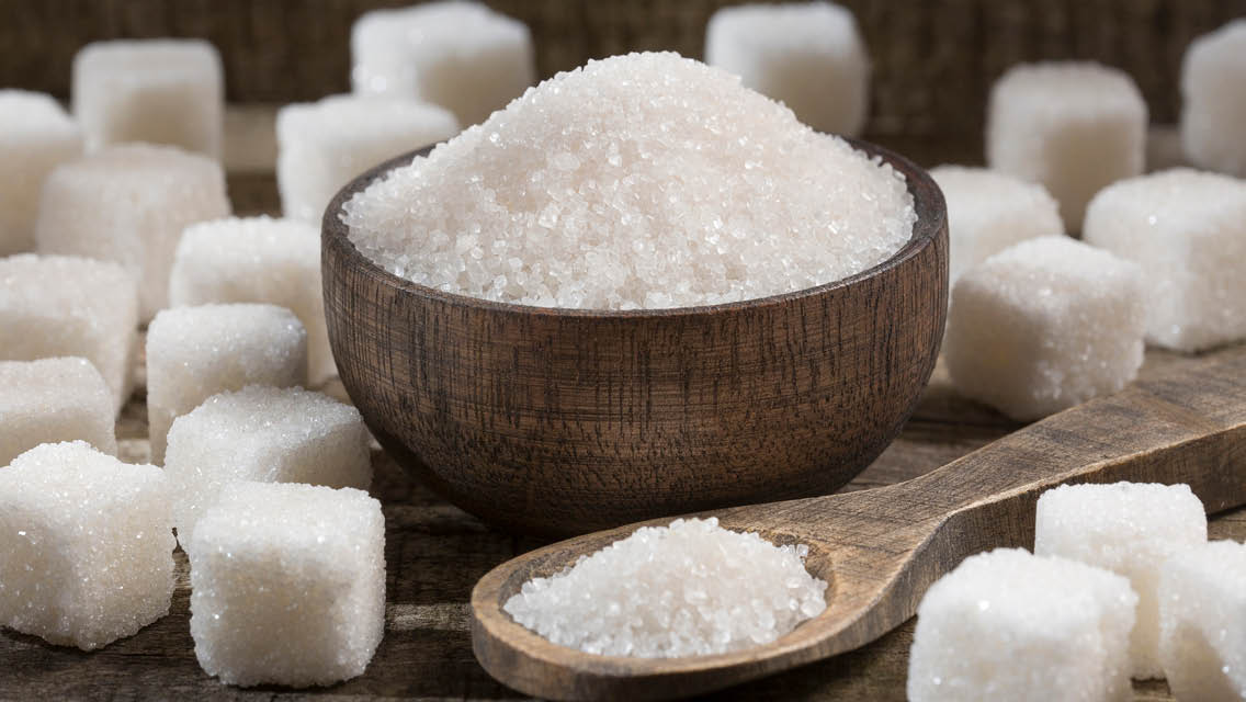 a wooden bowl filled with sugar surrounded by sugar cubes