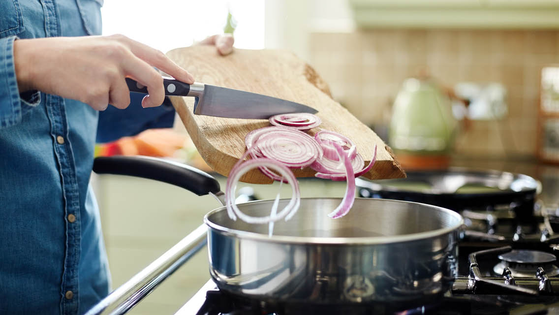 a person slides slices of onion off a cutting board into a put of water