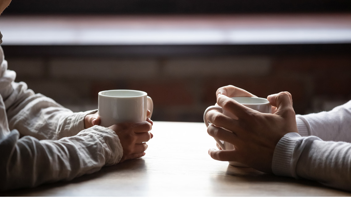 hands holding mugs across a table from each other