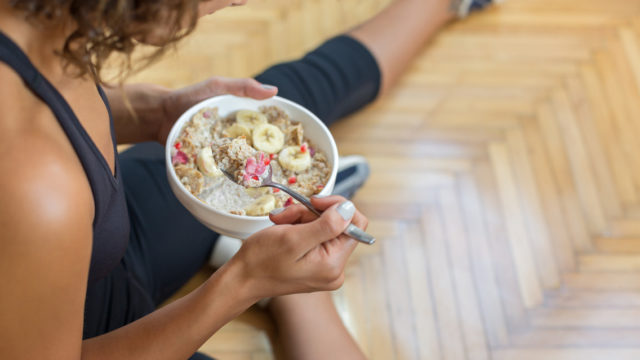 a woman sits on the floor while eating a bowl of oatmeal with fresh fruit