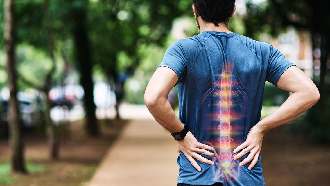 a man holds his low back with an illustration of the spine overlaid