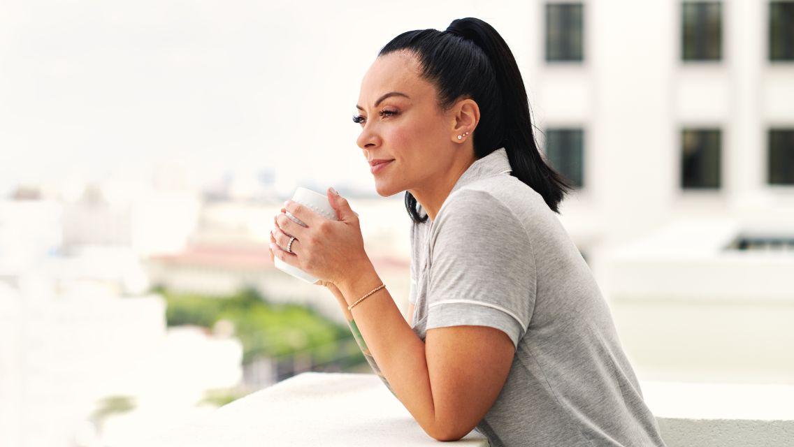 A woman drinking a cup of coffee while looking out over her balcony.