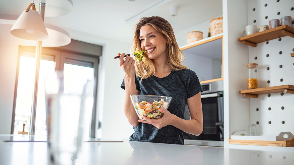 a woman smiles while enjoying a fresh salad in her kitchen
