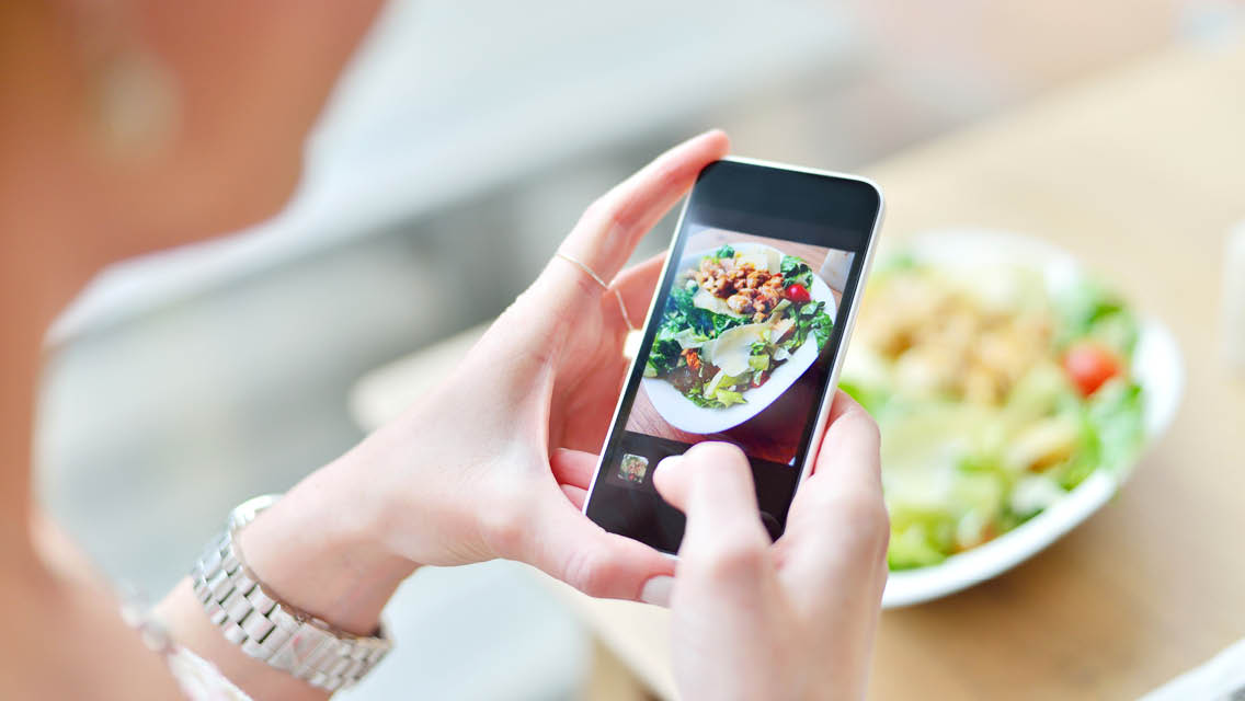 a woman looks at her phone with the image of a salad on it