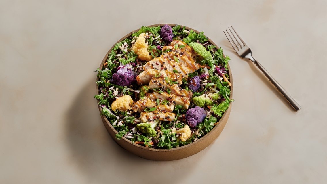 A bowl with chicken, cauliflower, greens, and other healthy ingredients.