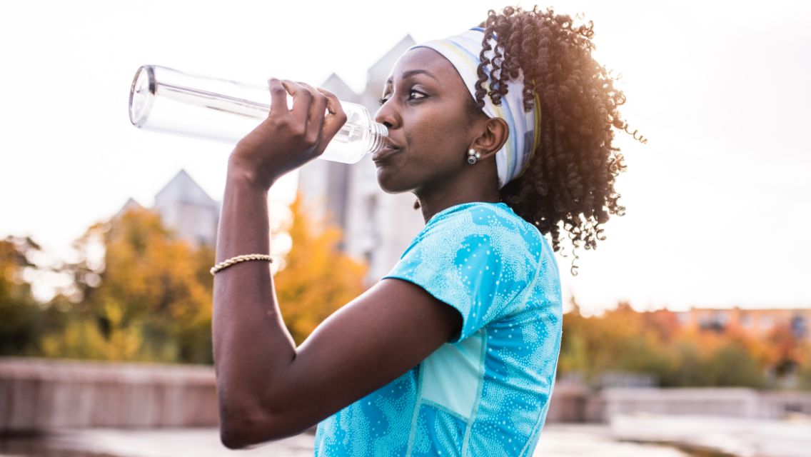A woman drinking out of a water bottle while on a walk outside.