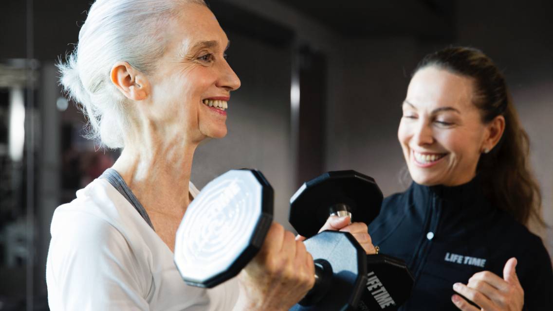 A Life Time trainer coaching a gray-haired woman using dumbbells.