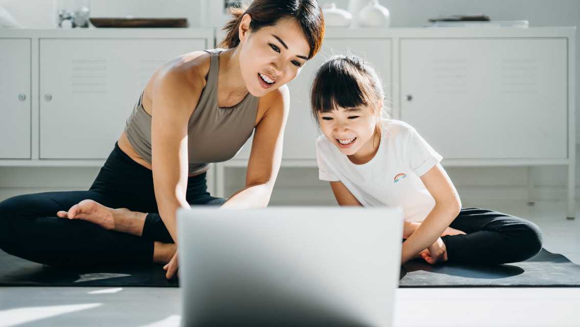 A mother and daughter at home in workout clothing looking at a laptop.
