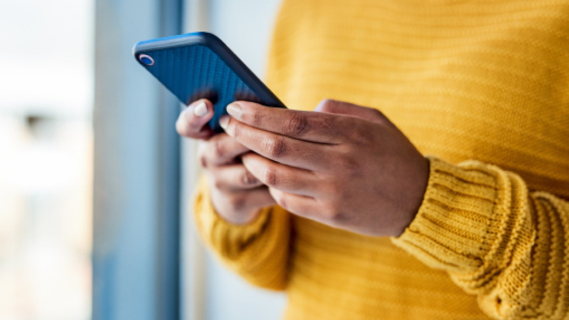 a person in a yellow sweater holds a cell phone