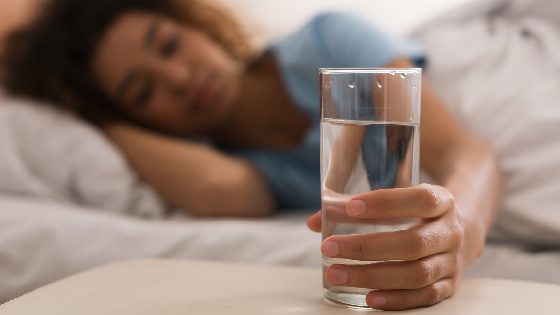 a woman lies in bed while clutching a glass of water