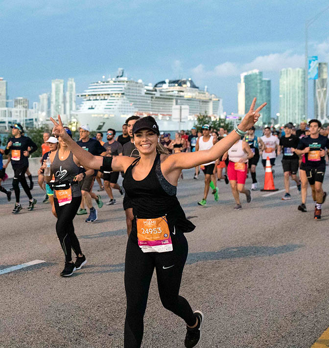 A woman in front of a group of runners all racing in the Miami Marathon.