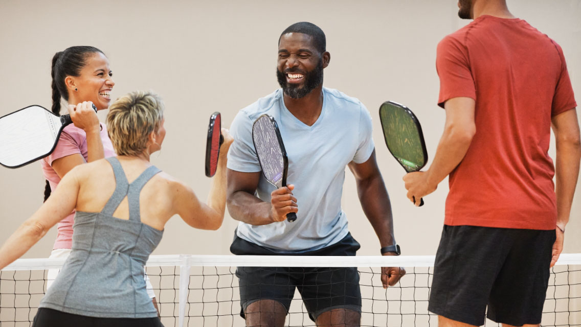 A group of four individuals smiling while playing pickleball.