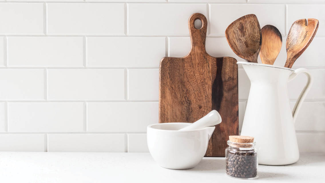 a cutting board, pitcher with wooden spoons and ceramic bowl on a kitchen counter