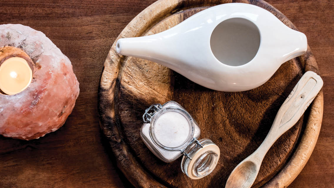 a neti pot sits on a wooden tray with salt and a spoon