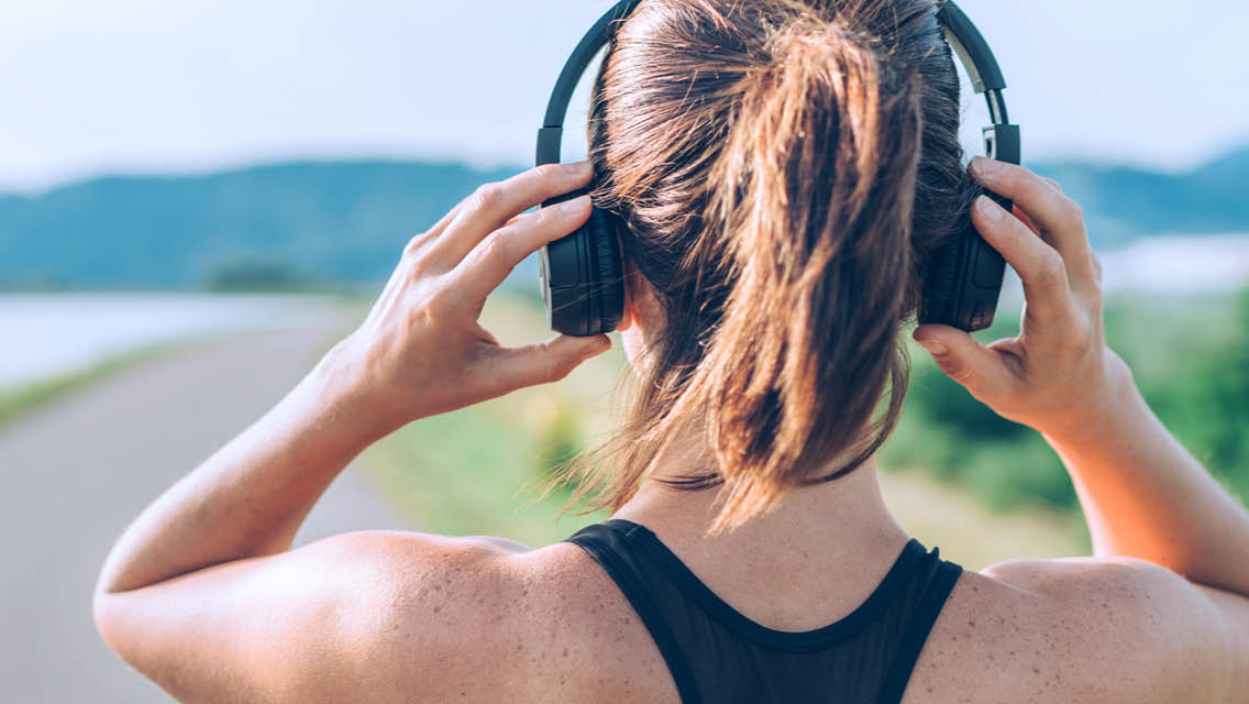 a woman looks at a running trail while adjusting headphone
