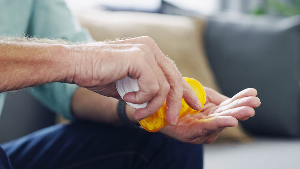 a senior man dumps pills from a pill bottle into his hand