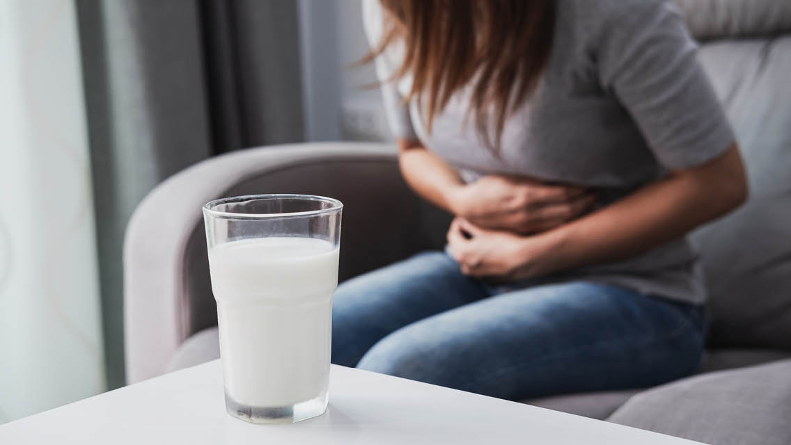 a glass of milk sits on a table with a woman holding her arms around her stomach
