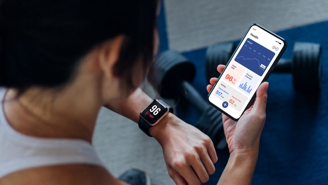 A woman looking at her Apple Watch and her phone for heart-rate and activity metics.