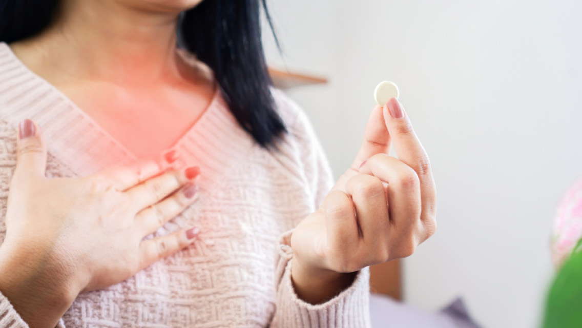 a woman presses her chest while holding an antacid