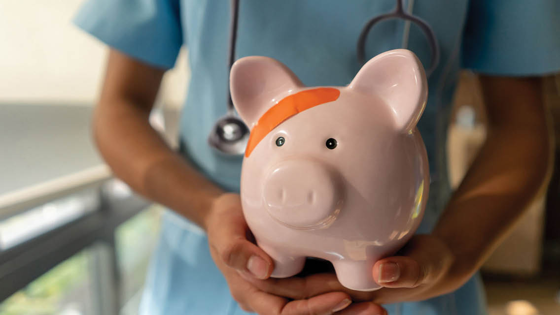A medical professional holds a piggy bank that has a band-aid on its head.