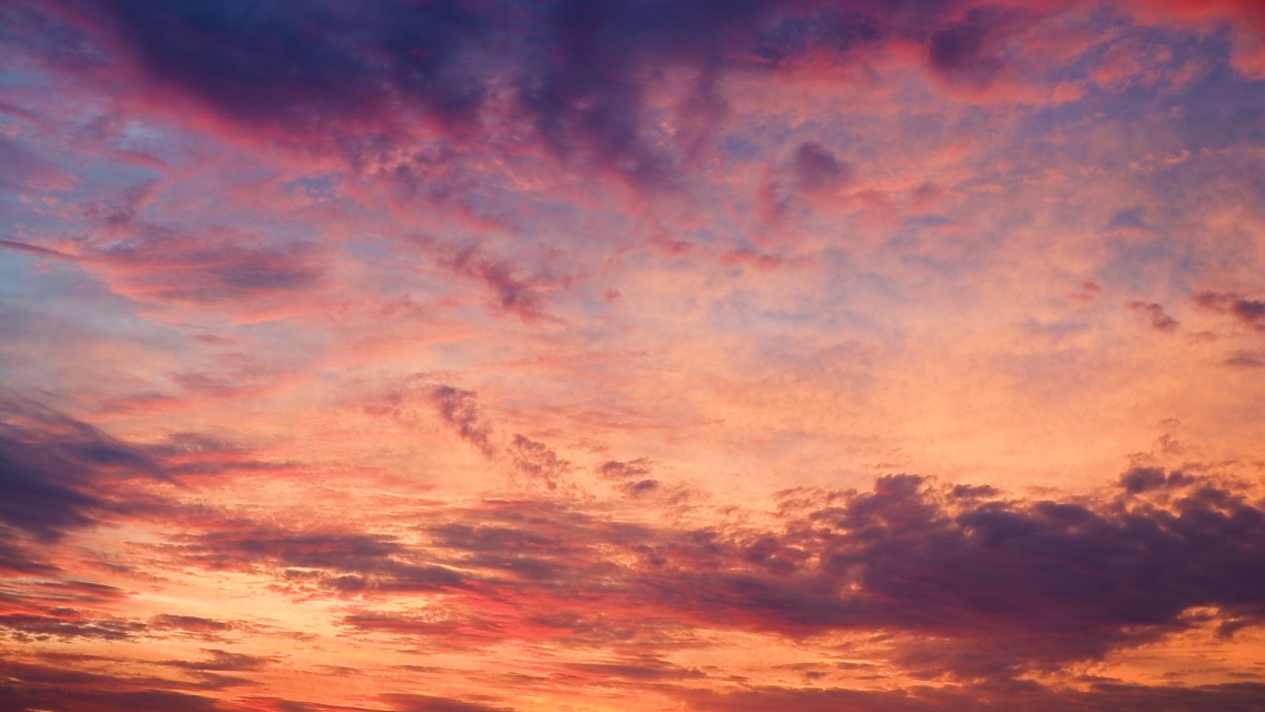 A sky during sunset, featuring clouds and shades of pinks, purples, oranges, and yellows.