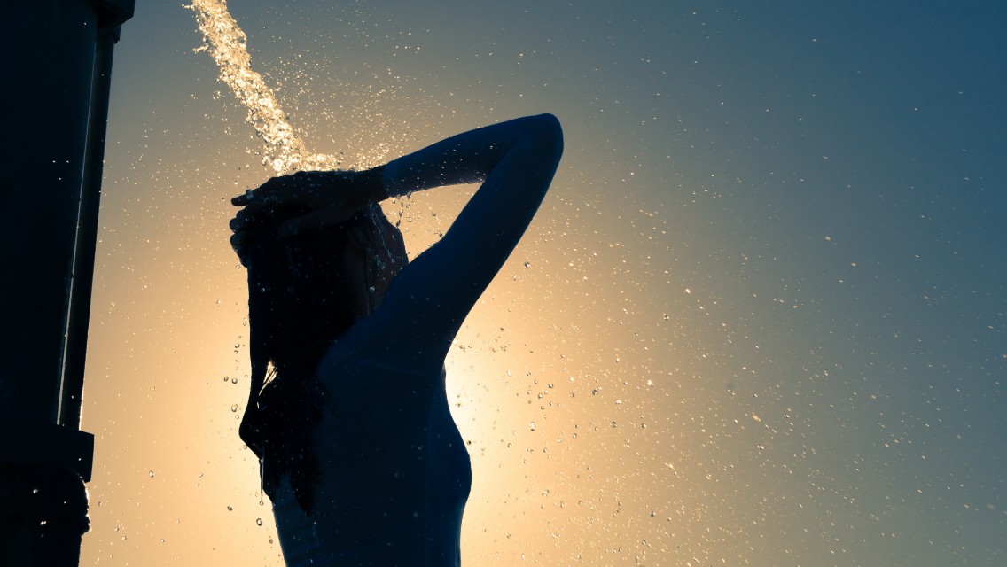 A woman rinsing her hair with water outdoors.