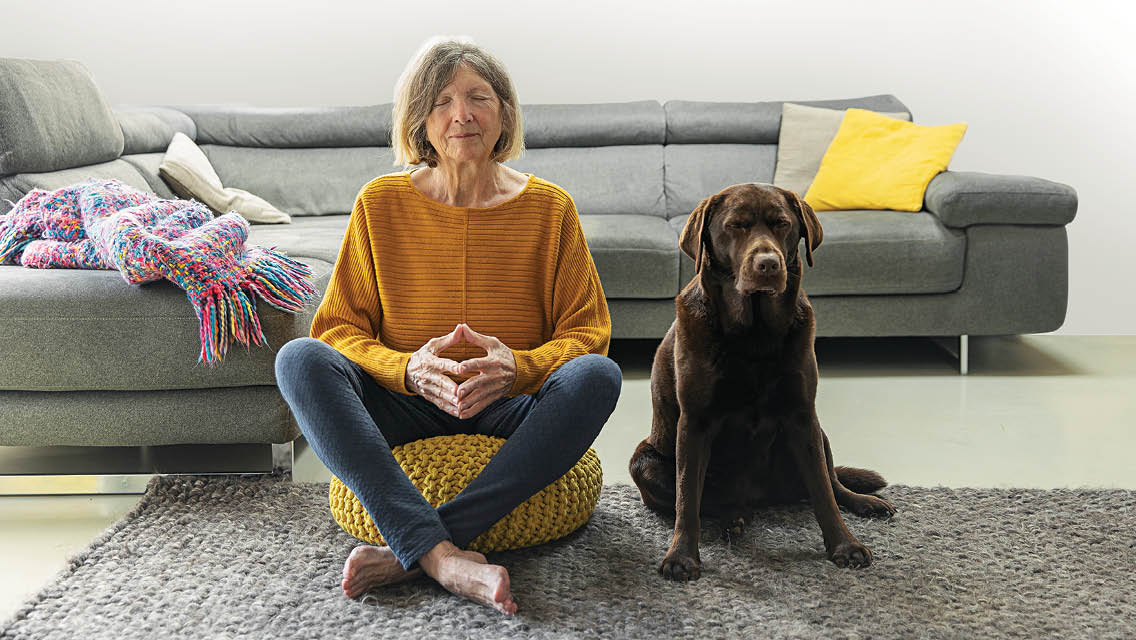 a woman sits on a meditation cushion with her chocolate lab next to her