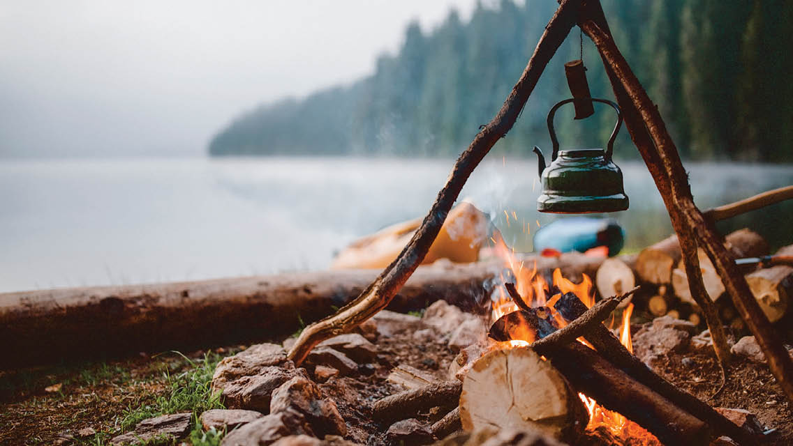 a tea kettle hangs over an open campfire