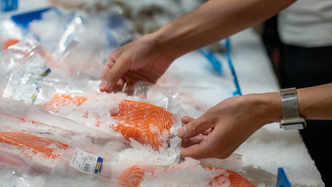 a person selects a salmon filet from an ice filled counter