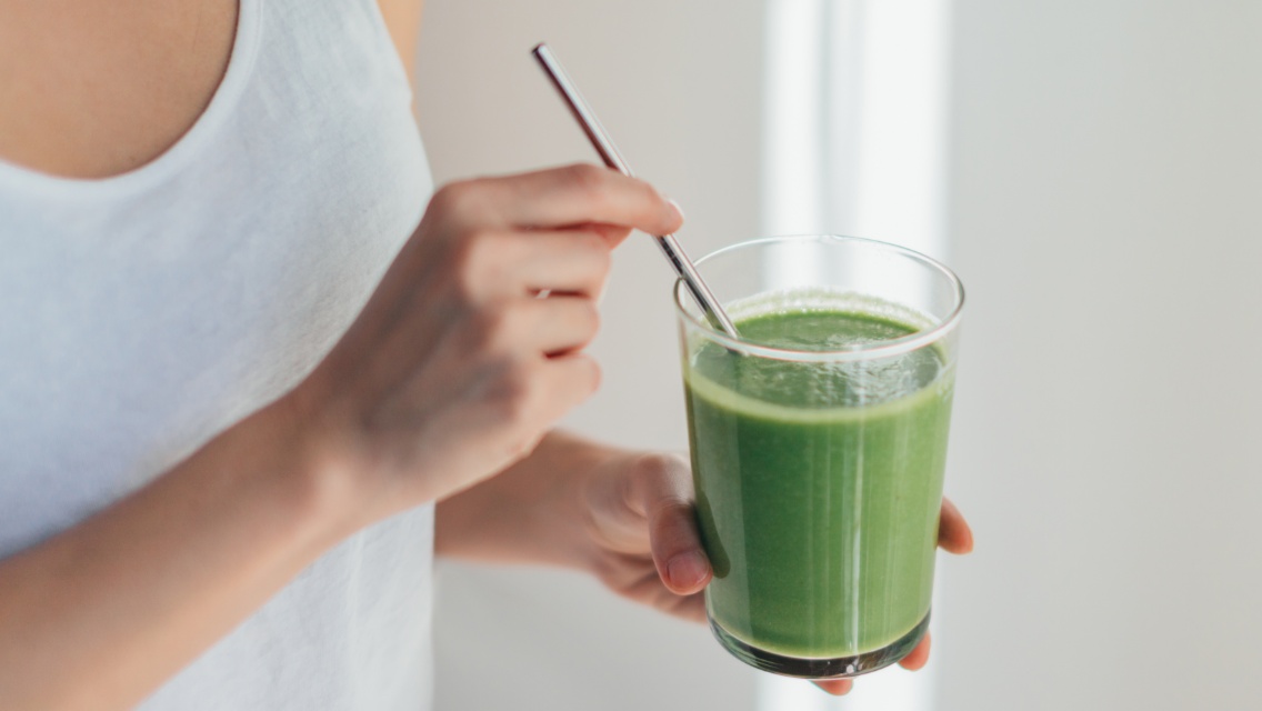 A woman holding a green smoothie.