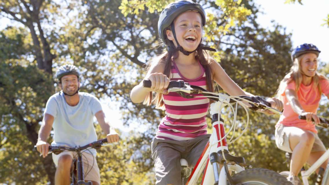 A father, mother and daughter smiling while bike riding together outside.